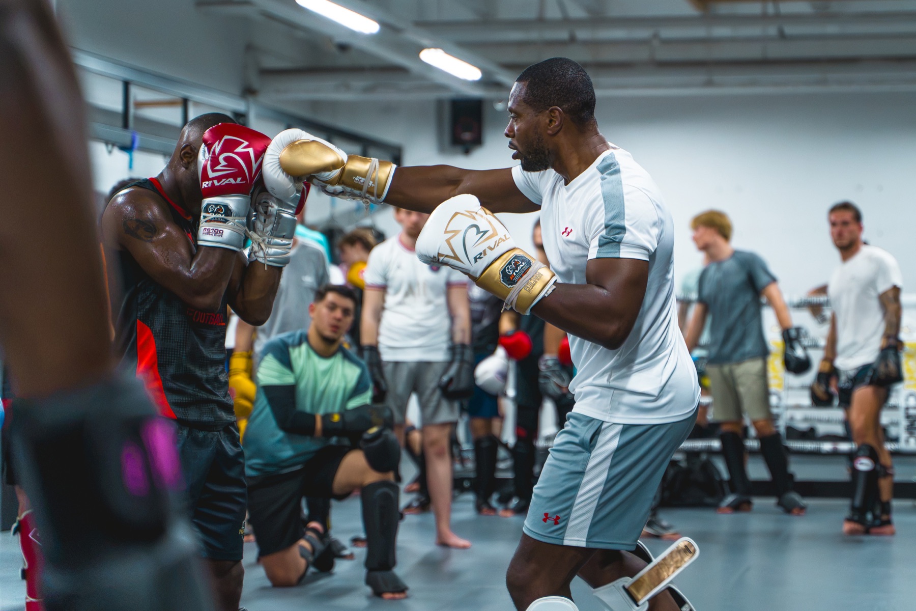 Een deelnemer zit geknield op de mat tijdens een training met pads.